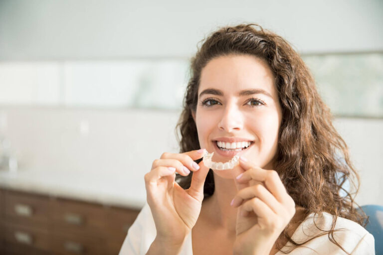 Mulher jovem sorri segurando um aparelho invisível transparente, mostrando a discrição do tratamento ortodôntico na Sculpere em Campinas.