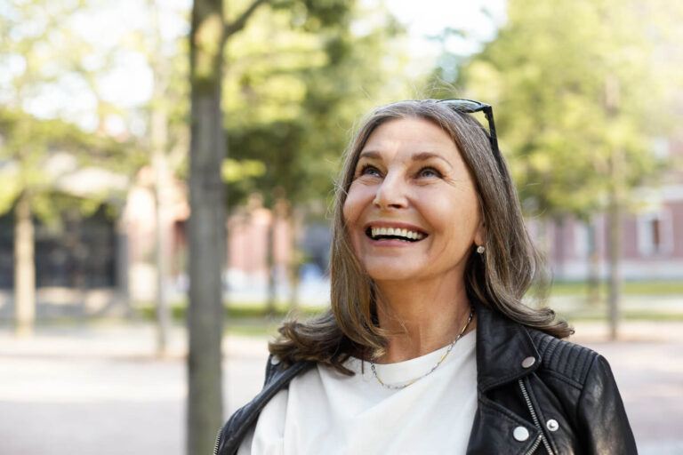 Mulher madura sorrindo ao ar livre com dentes alinhados e fixos, resultado da técnica All-on-4 realizada na Sculpere em Campinas.