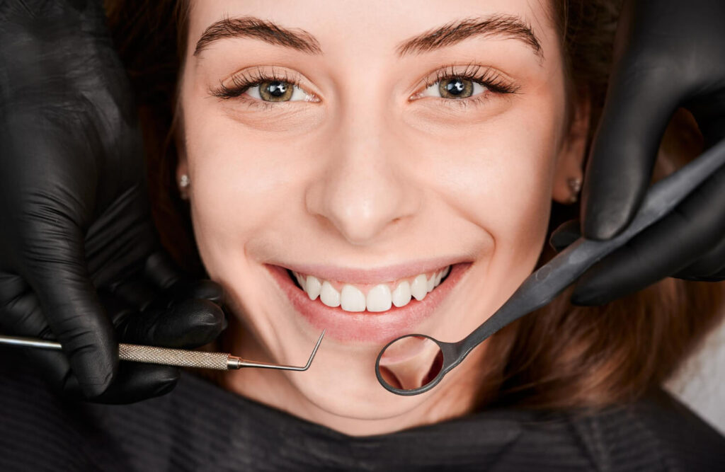 Paciente sorrindo em avaliação na Sculpere, clínica para colocar prótese dentária em Campinas, enquanto dentista segura espelho clínico.