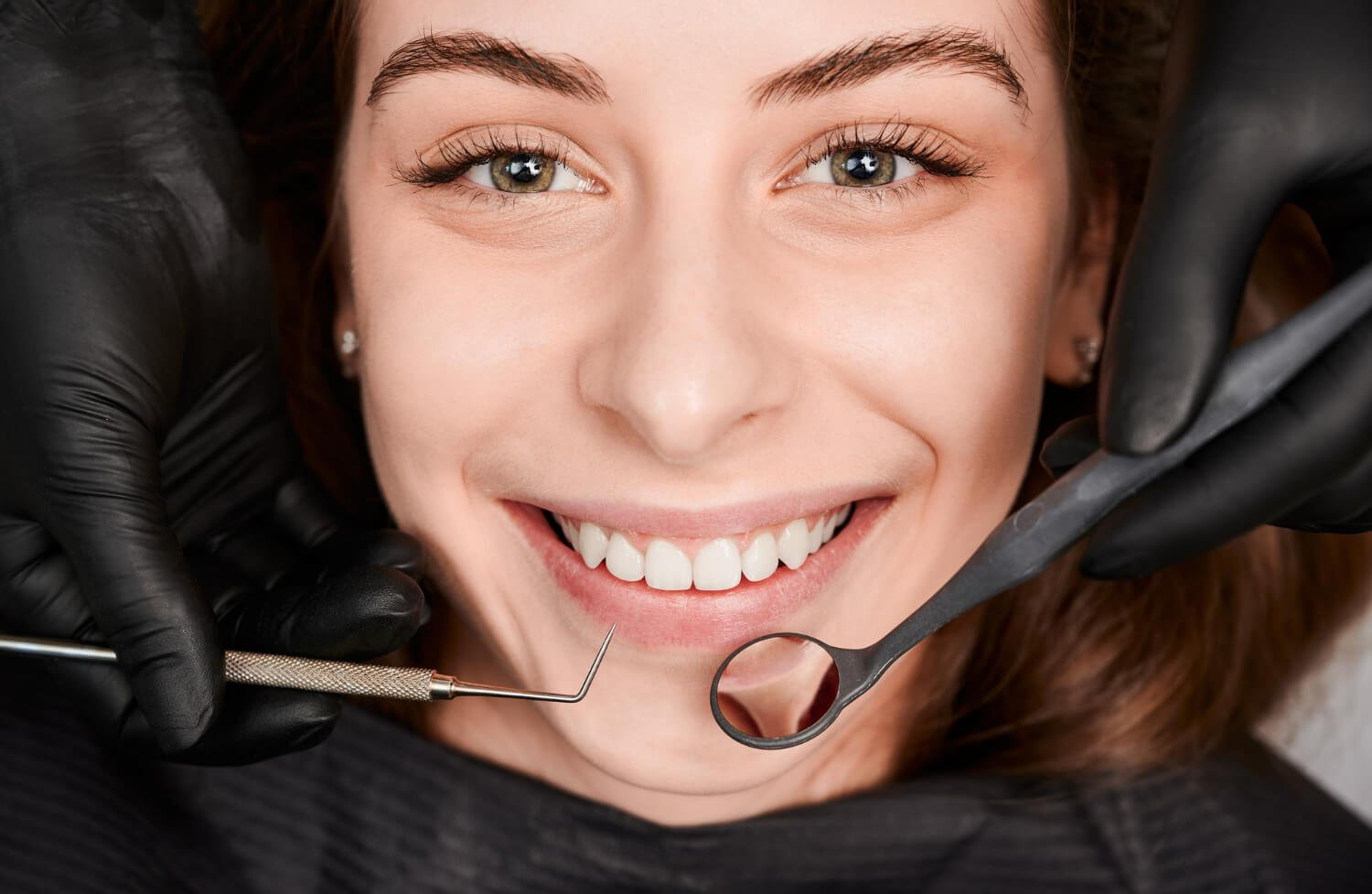 Paciente sorrindo em avaliação na Sculpere, clínica para colocar prótese dentária em Campinas, enquanto dentista segura espelho clínico.