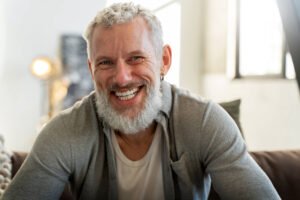 Homem sênior de barba grisalha sorrindo com conforto após ajuste de prótese dentária machucando na Sculpere em Nova Campinas.