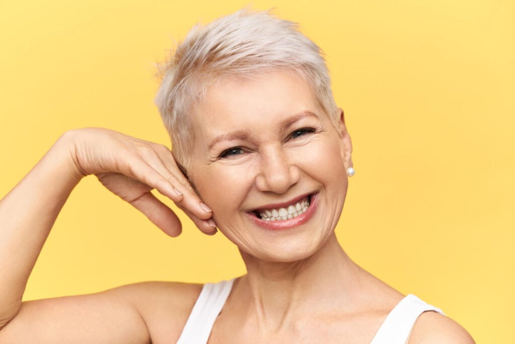Mulher idosa e sorridente toca o rosto, demonstrando o conforto e a rápida adaptação com sua nova prótese dentária em Campinas.