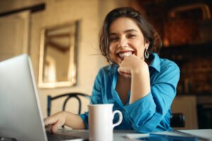 Mulher jovem sorrindo em frente ao laptop, mostrando a praticidade e conforto na rotina com alinhadores invisíveis em Nova Campinas.